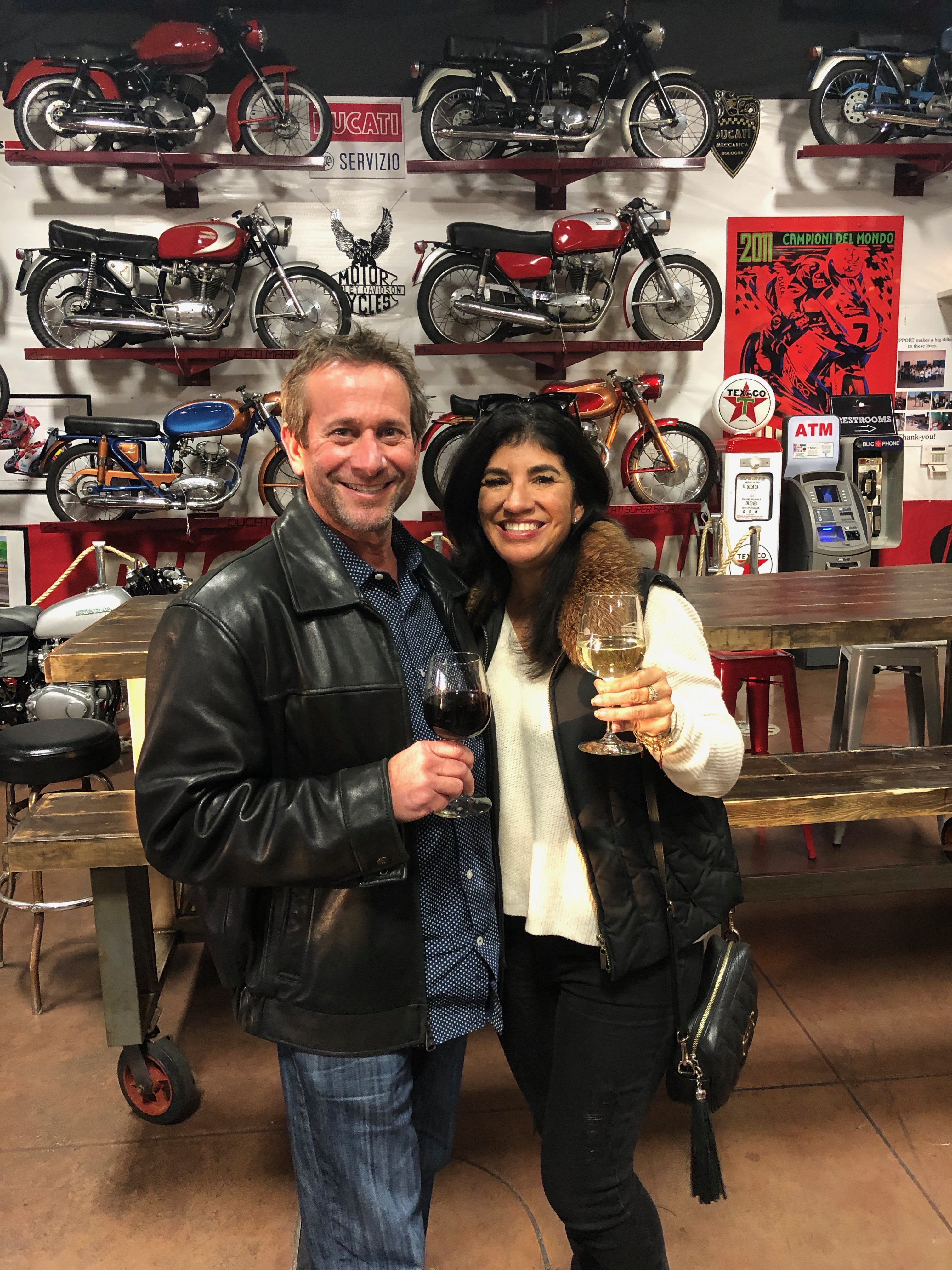 David and Kandi with wineglasses beneath vintage motorcycles